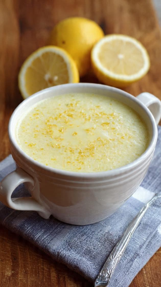 Creamy lemon soup topped with zest in a white mug, with fresh lemons behind.
