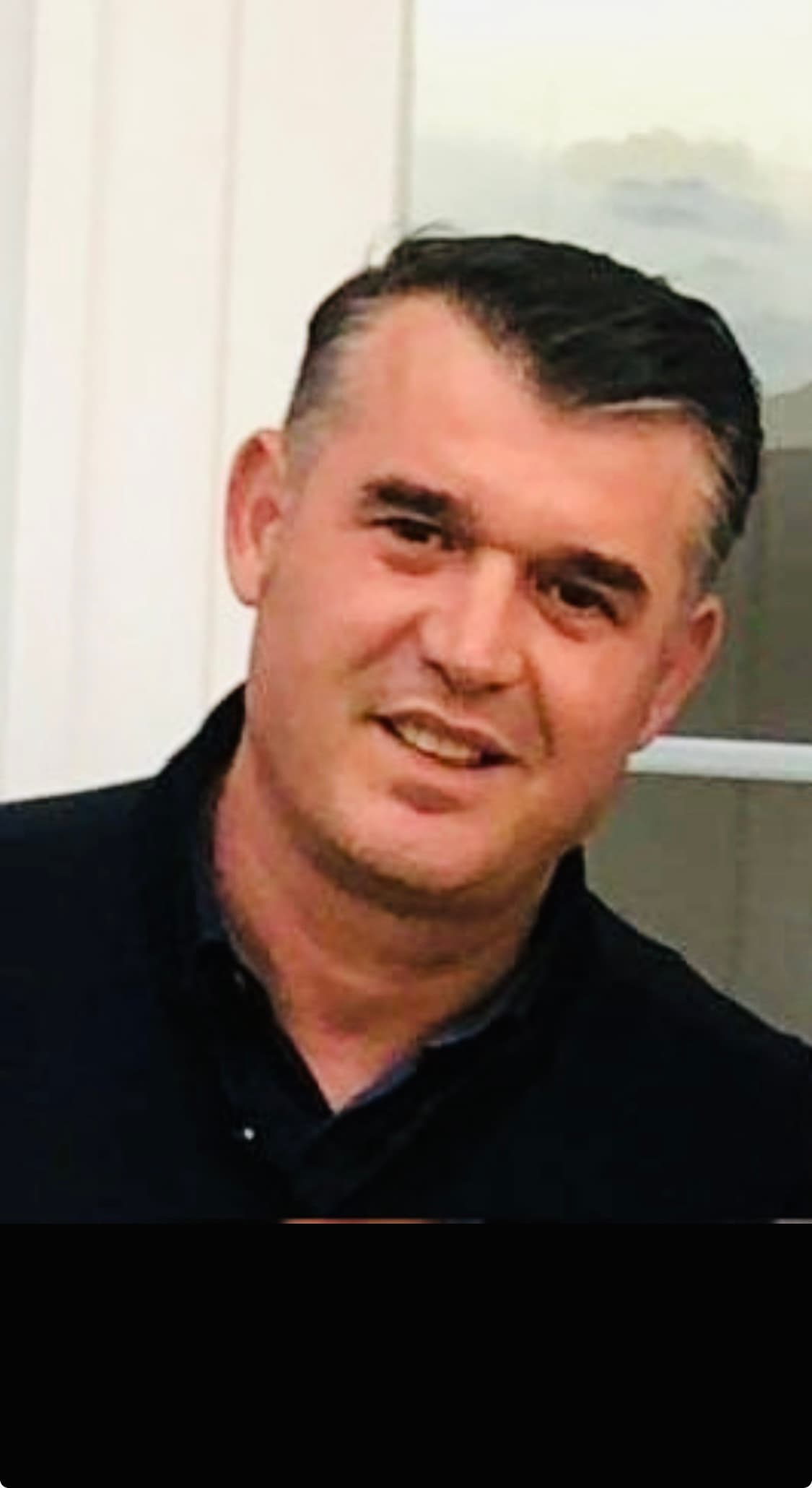 Smiling middle-aged man with short dark hair wearing a dark collared shirt.