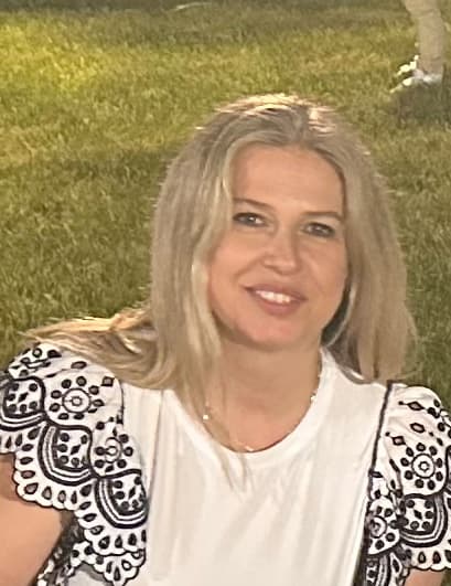 Smiling blonde woman wearing a white top with black and white eyelet ruffled sleeves.