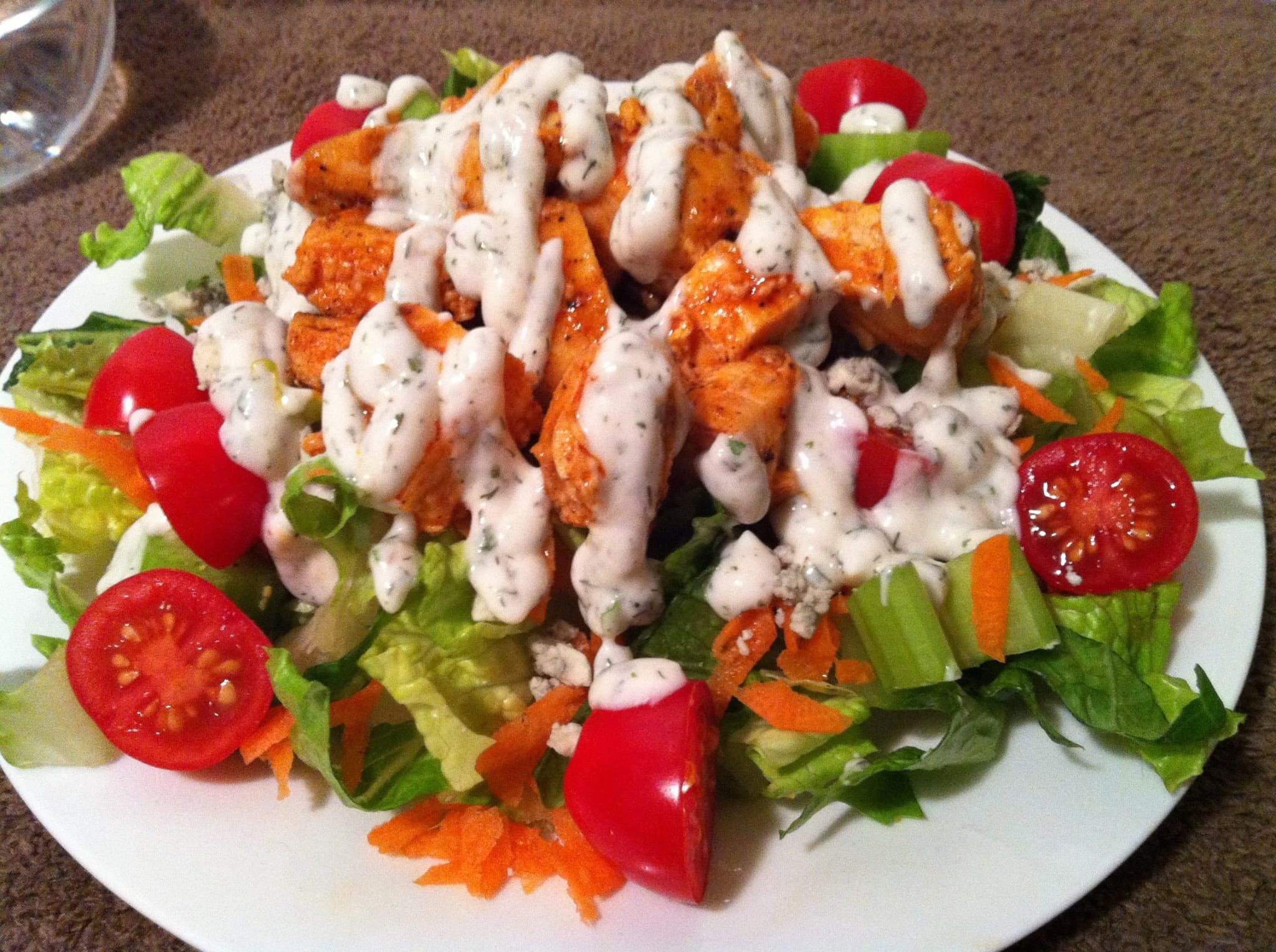 Buffalo chicken salad with cherry tomatoes, carrots, and celery, drizzled with creamy ranch dressing.