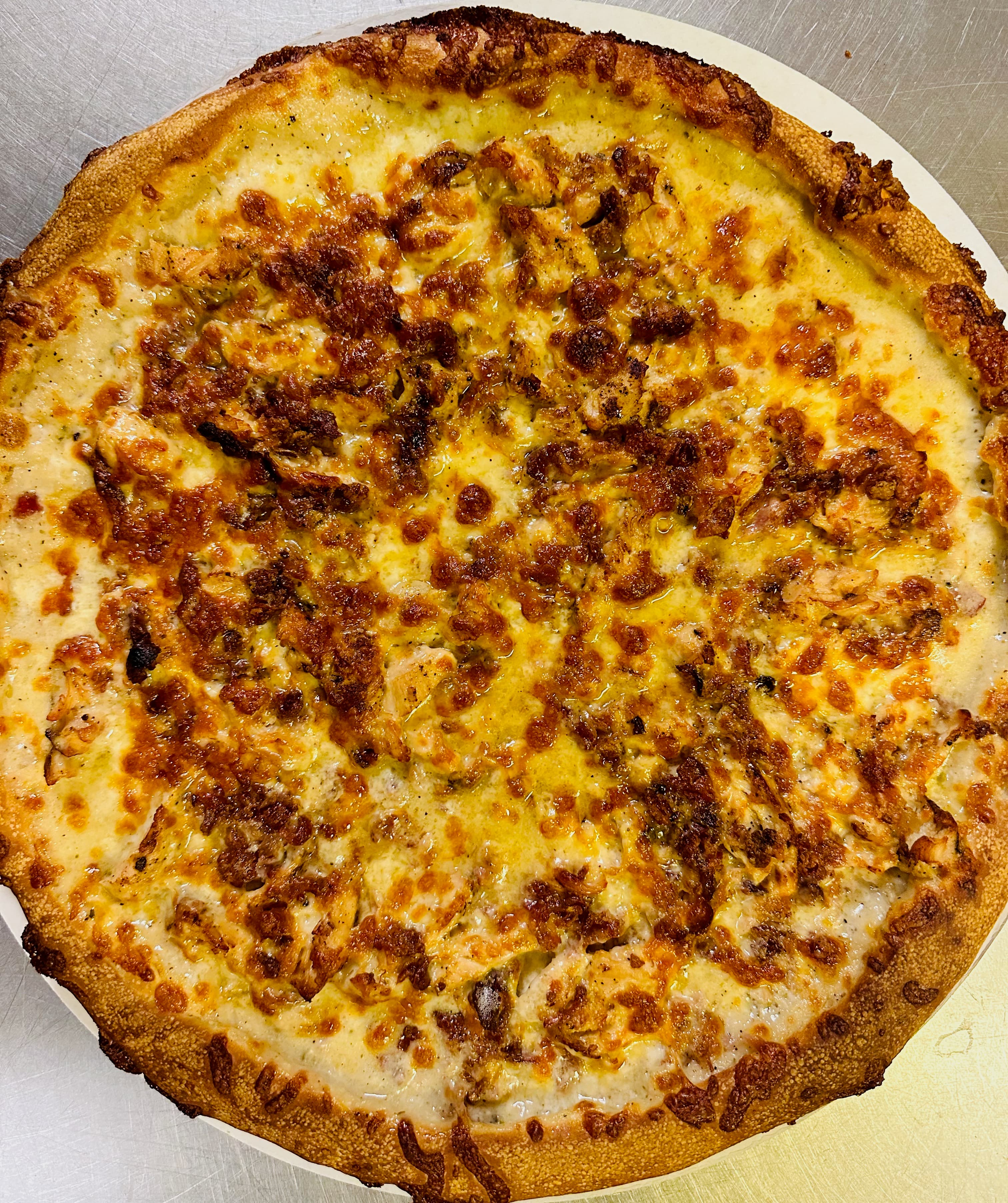 Golden-brown pizza with thick crust, white sauce, bubbly melted cheese, and shredded meat toppings.