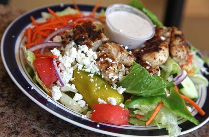 Grilled chicken salad with feta cheese, fresh vegetables, and a side of creamy white dressing.
