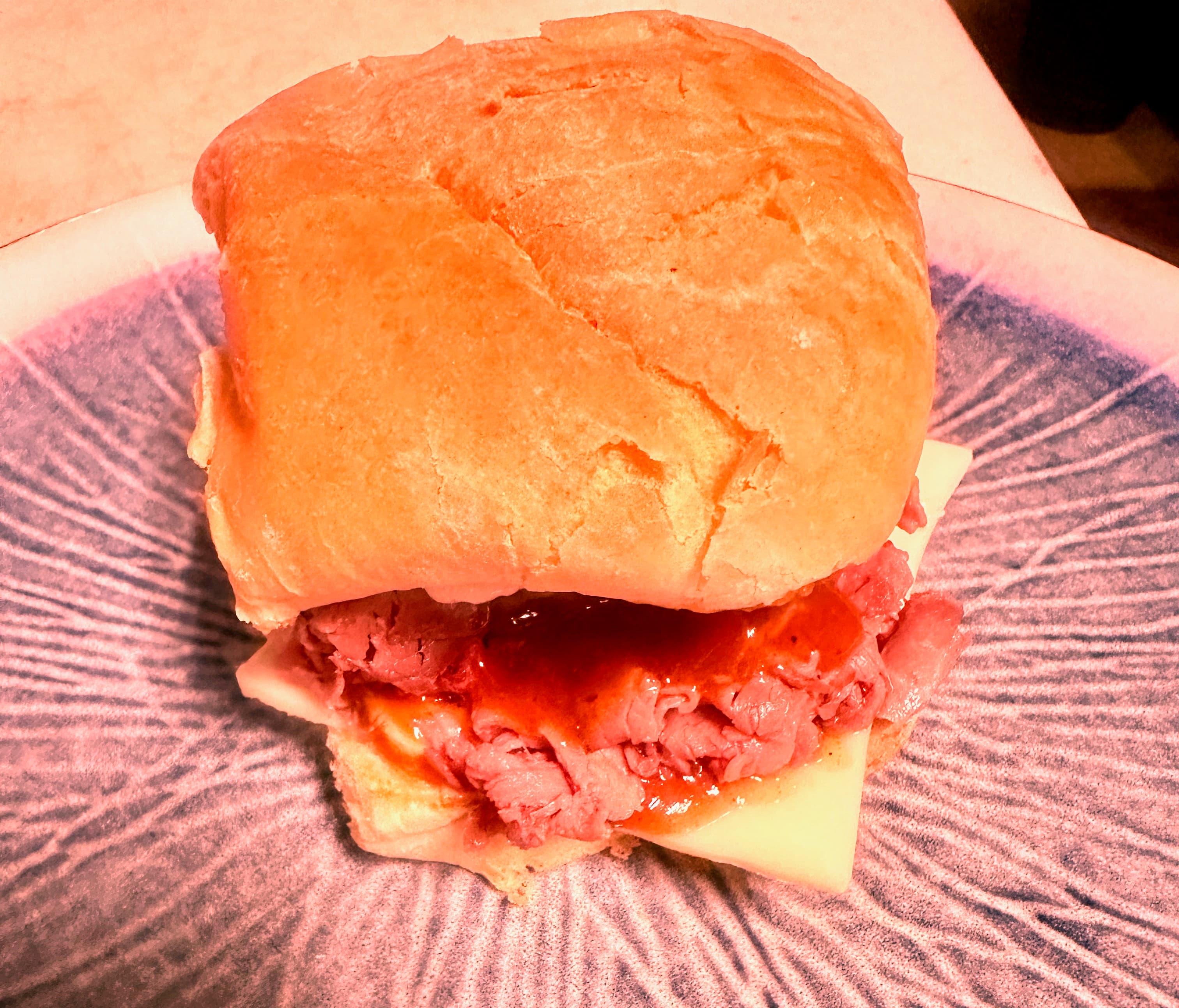 Roast beef sandwich with cheese and red sauce on a crusty bun on blue plate.