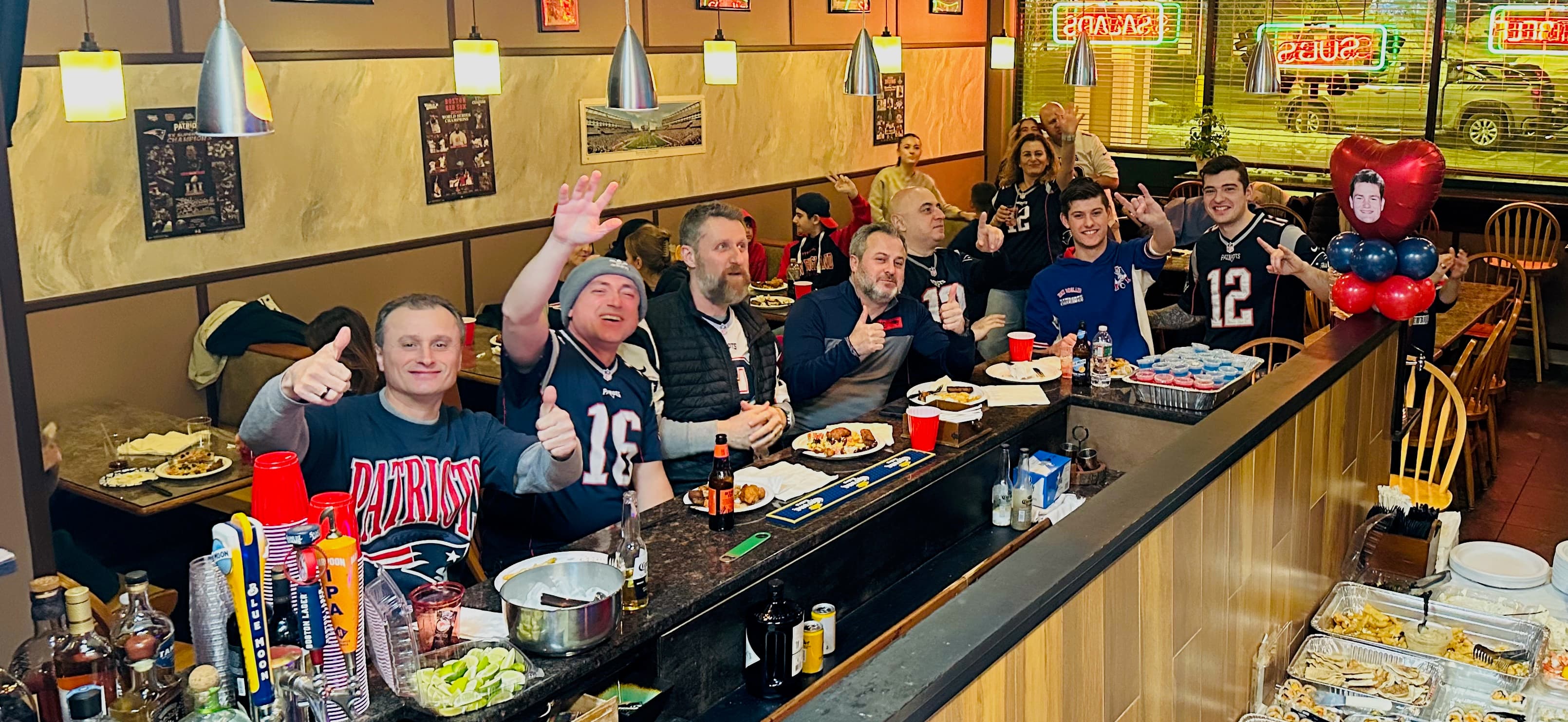 New England Patriots fans cheering and giving thumbs up at a restaurant bar counter.