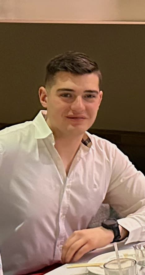 Young man with short dark hair wearing a white button-down shirt and a black watch.