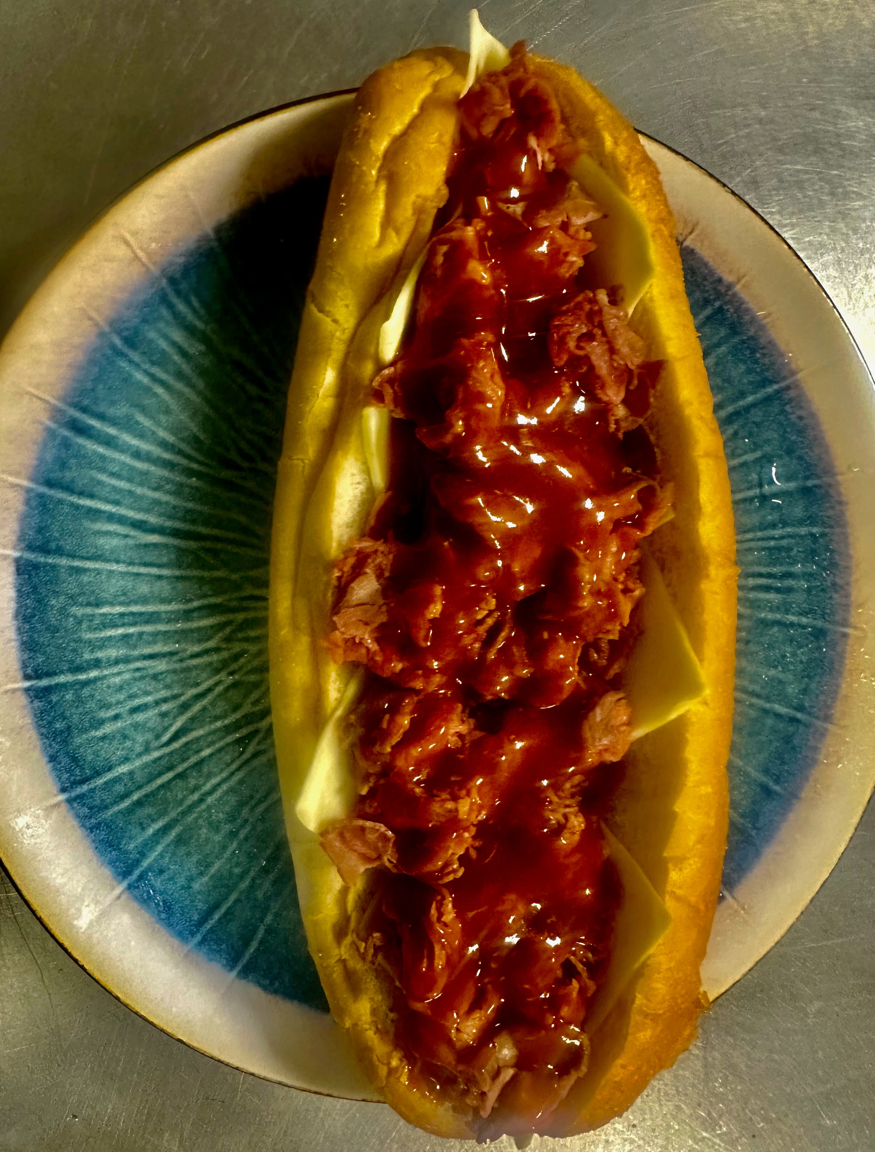 Pulled meat sub with cheese and red sauce on a blue and white patterned plate.